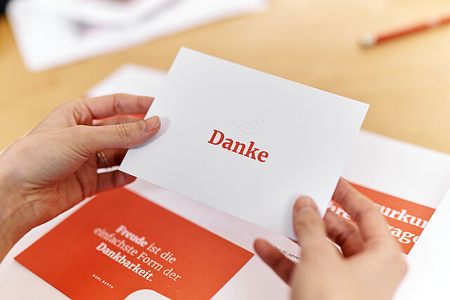 Symbolfoto Mappe mit Dokumenten des DRK (Dankesurkunde). Hände halten eine Karte mit einer Danksagung - 2021