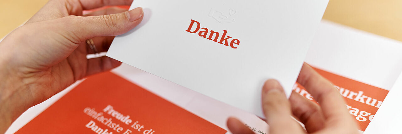 Symbolfoto Danksagung des DRK Symbolfoto Mappe mit Dokumenten des DRK (Dankesurkunde). Hände halten eine Karte mit einer Danksagung - 2021